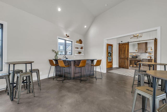 interior space featuring a kitchen bar, a barn door, high vaulted ceiling, kitchen peninsula, and backsplash