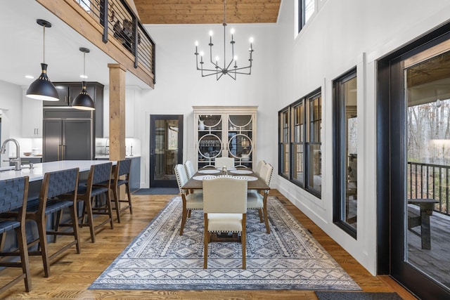 dining space with hardwood / wood-style flooring, a towering ceiling, sink, and an inviting chandelier