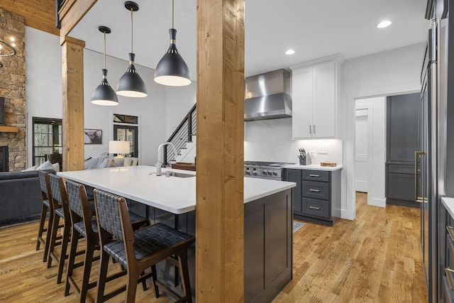 kitchen with wall chimney range hood, sink, a breakfast bar, white cabinetry, and decorative light fixtures