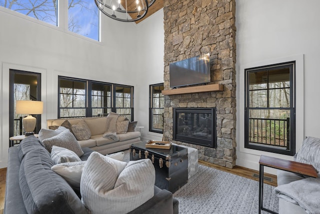 living room with hardwood / wood-style floors, a stone fireplace, a chandelier, and a towering ceiling