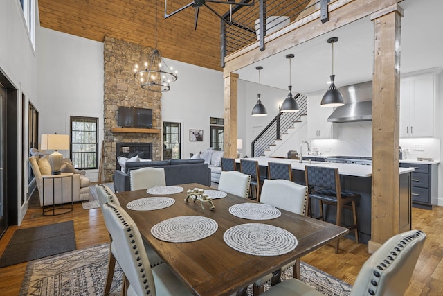 dining space with an inviting chandelier, wooden ceiling, a fireplace, light hardwood / wood-style floors, and a high ceiling