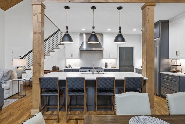 kitchen with wall chimney exhaust hood, sink, gray cabinetry, hanging light fixtures, and white cabinets