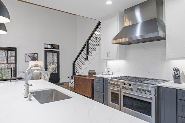 kitchen featuring range hood, sink, white cabinets, range with two ovens, and light stone countertops