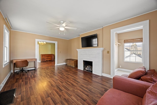 living room featuring dark wood-type flooring, ceiling fan with notable chandelier, and a brick fireplace