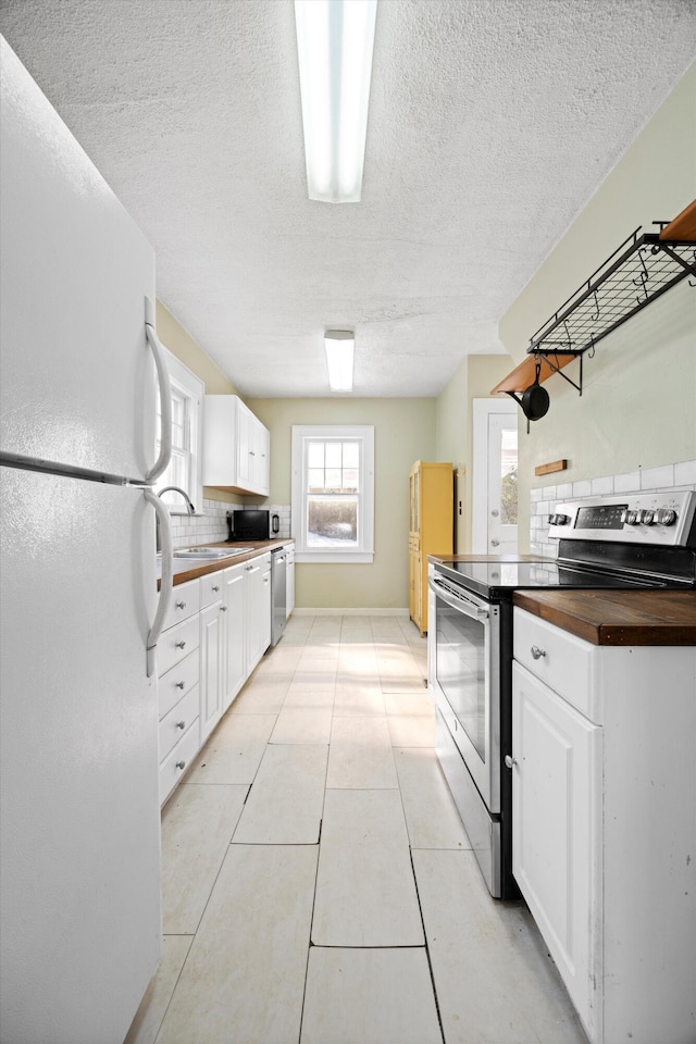 kitchen featuring white cabinets, butcher block countertops, backsplash, and appliances with stainless steel finishes