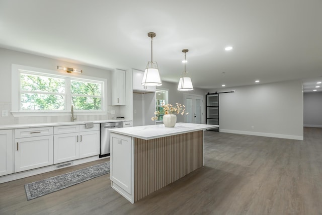 kitchen with a barn door, backsplash, a kitchen island, stainless steel dishwasher, and white cabinetry