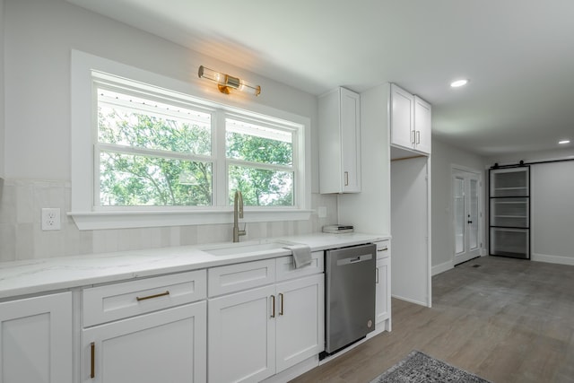 kitchen with dishwasher, white cabinetry, sink, light stone counters, and a barn door