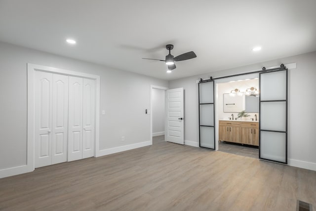 unfurnished bedroom with ensuite bath, light hardwood / wood-style floors, a closet, ceiling fan, and a barn door