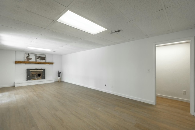 unfurnished living room with a drop ceiling, a brick fireplace, and hardwood / wood-style floors