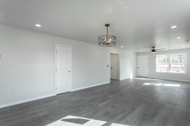 empty room featuring ceiling fan with notable chandelier and dark hardwood / wood-style floors