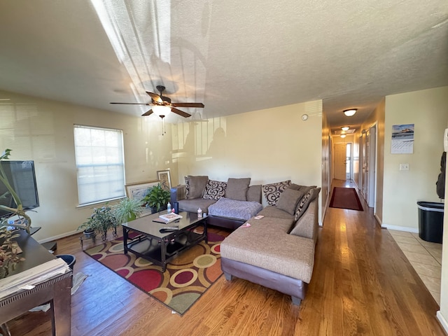 living room with a textured ceiling, ceiling fan, and light hardwood / wood-style flooring