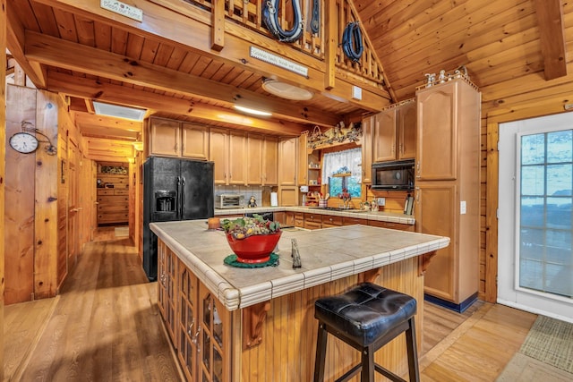 kitchen with black appliances, a kitchen island, light hardwood / wood-style floors, backsplash, and tile countertops