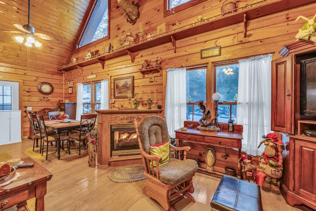 living room featuring ceiling fan, high vaulted ceiling, wood walls, and a healthy amount of sunlight