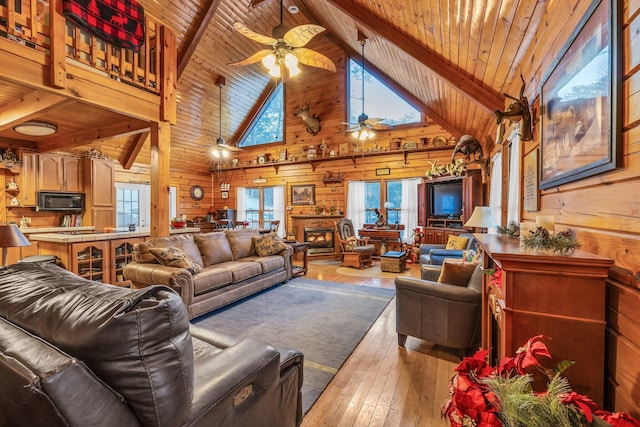 living room with high vaulted ceiling, light wood-type flooring, wooden walls, and ceiling fan