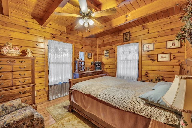 bedroom with light wood-type flooring, ceiling fan, beam ceiling, and wooden walls