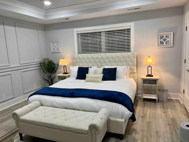 bedroom with a raised ceiling, crown molding, and hardwood / wood-style floors