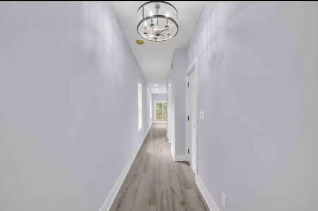 hallway with light wood-type flooring and a notable chandelier