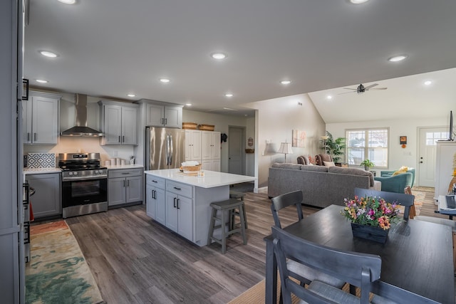 kitchen featuring appliances with stainless steel finishes, gray cabinetry, decorative backsplash, lofted ceiling, and wall chimney range hood