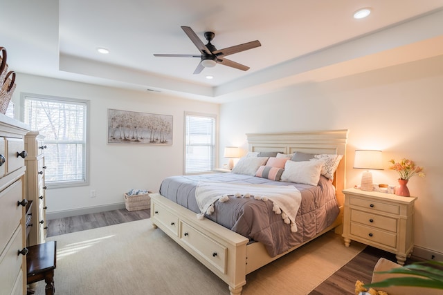 bedroom with ceiling fan, a tray ceiling, and light hardwood / wood-style flooring