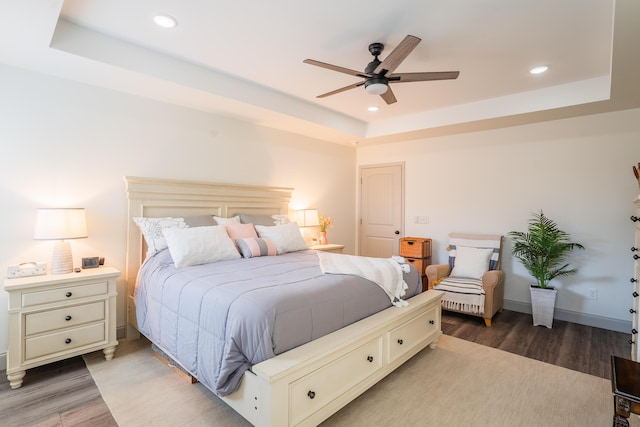 bedroom with a raised ceiling, ceiling fan, and dark hardwood / wood-style flooring