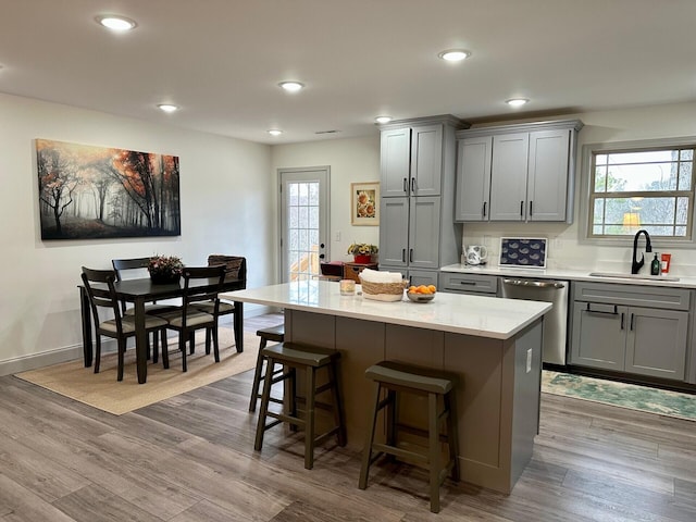 kitchen with stainless steel dishwasher, light hardwood / wood-style flooring, sink, and a center island