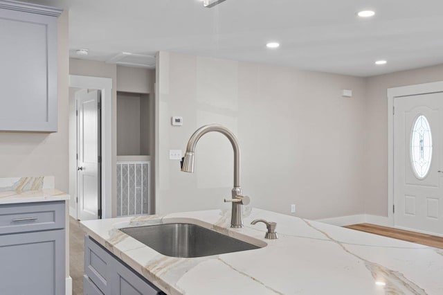 kitchen with light stone countertops, sink, gray cabinets, and light hardwood / wood-style flooring