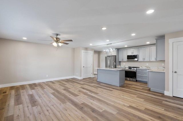 kitchen with pendant lighting, appliances with stainless steel finishes, gray cabinets, and an island with sink