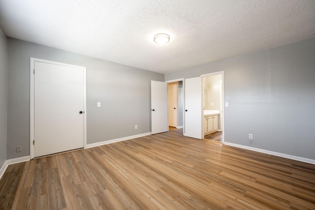 unfurnished bedroom with a textured ceiling, a closet, ensuite bathroom, and wood-type flooring