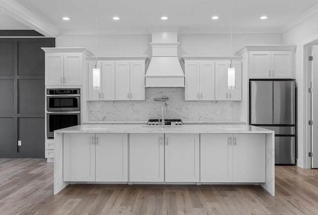 kitchen with pendant lighting, white cabinets, appliances with stainless steel finishes, custom exhaust hood, and a kitchen island with sink