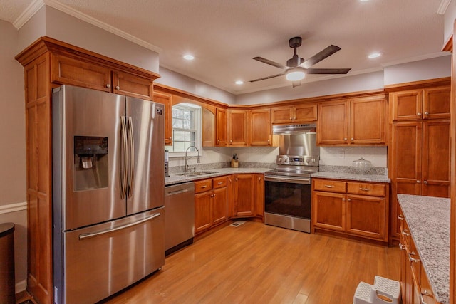 kitchen with brown cabinetry, appliances with stainless steel finishes, light wood-type flooring, and a sink