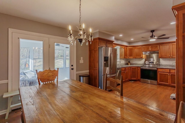 kitchen featuring ceiling fan with notable chandelier, a sink, appliances with stainless steel finishes, brown cabinetry, and light wood finished floors