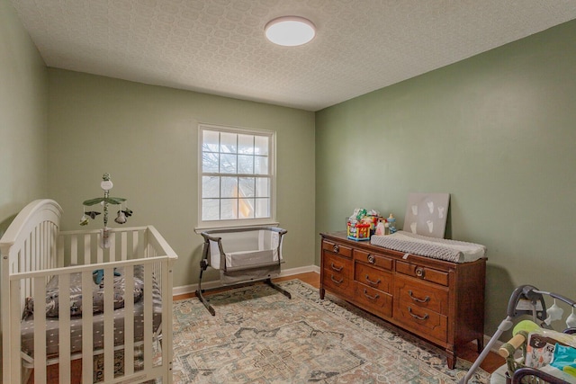 bedroom featuring a textured ceiling, baseboards, a nursery area, and light wood finished floors