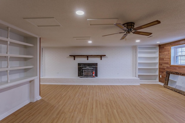 unfurnished living room with built in shelves, a textured ceiling, wood finished floors, a brick fireplace, and attic access