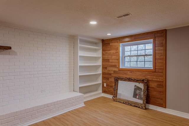 unfurnished living room featuring built in features, visible vents, light wood finished floors, a fireplace, and a textured ceiling