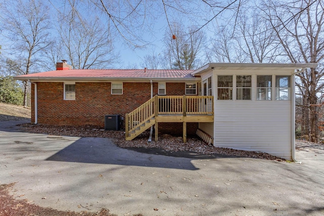 rear view of house with brick siding, stairway, cooling unit, and a chimney