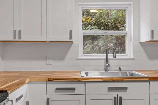 kitchen featuring backsplash, butcher block countertops, sink, white cabinetry, and range