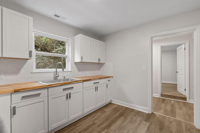 kitchen featuring white cabinets, wood-type flooring, butcher block counters, tasteful backsplash, and sink