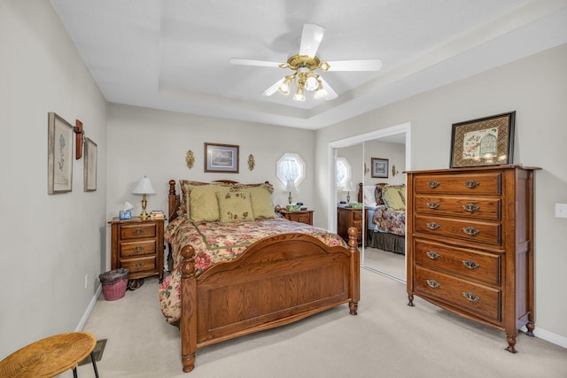 carpeted bedroom with ceiling fan and a tray ceiling