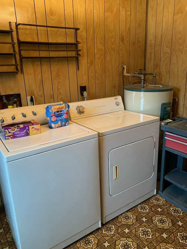 clothes washing area featuring electric water heater, washer and clothes dryer, and wooden walls