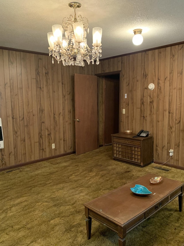 unfurnished room featuring a notable chandelier, wooden walls, a textured ceiling, and dark colored carpet