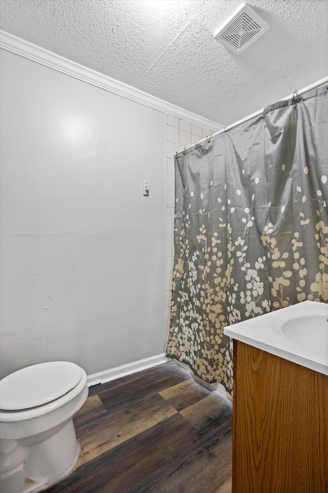 bathroom with toilet, a textured ceiling, hardwood / wood-style flooring, ornamental molding, and vanity