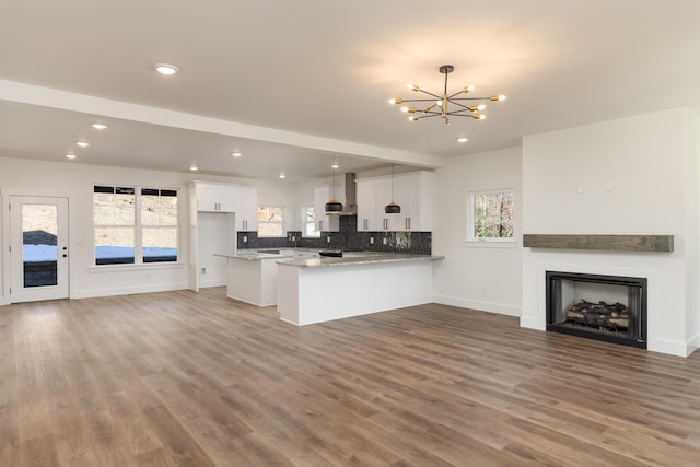 kitchen featuring decorative light fixtures, wall chimney range hood, kitchen peninsula, white cabinets, and a chandelier