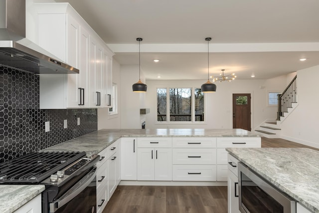 kitchen with wall chimney exhaust hood, decorative light fixtures, white cabinetry, light stone counters, and stainless steel range with gas stovetop