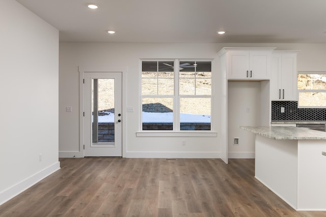 kitchen with decorative backsplash, dark hardwood / wood-style flooring, light stone countertops, stainless steel dishwasher, and white cabinets