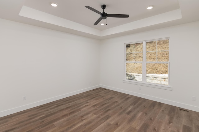 unfurnished room with ceiling fan, dark hardwood / wood-style floors, and a tray ceiling