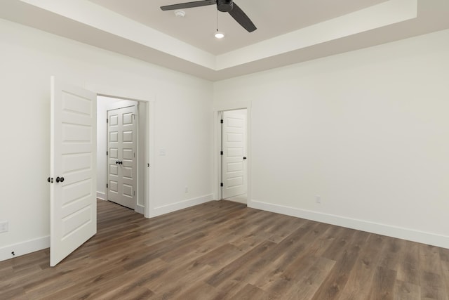 unfurnished bedroom with ceiling fan, dark wood-type flooring, and a raised ceiling