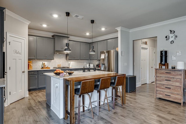 kitchen featuring gray cabinets, a breakfast bar, ornamental molding, a kitchen island with sink, and stainless steel appliances