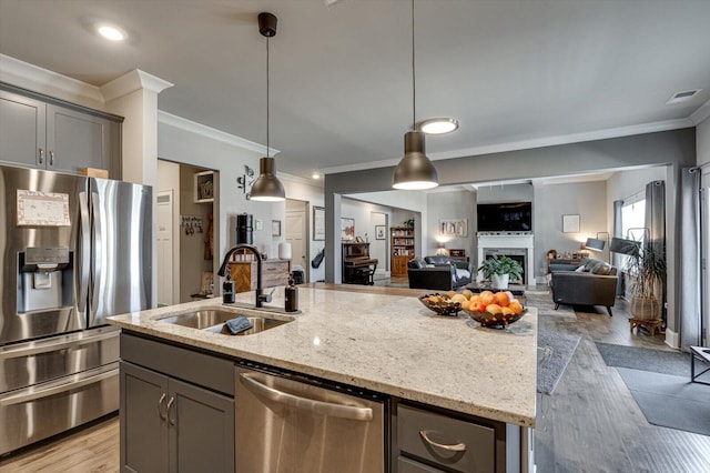 kitchen with stainless steel appliances, a kitchen island with sink, pendant lighting, and light stone counters