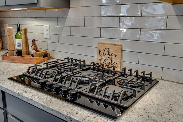 interior details with black gas stovetop, backsplash, and light stone counters