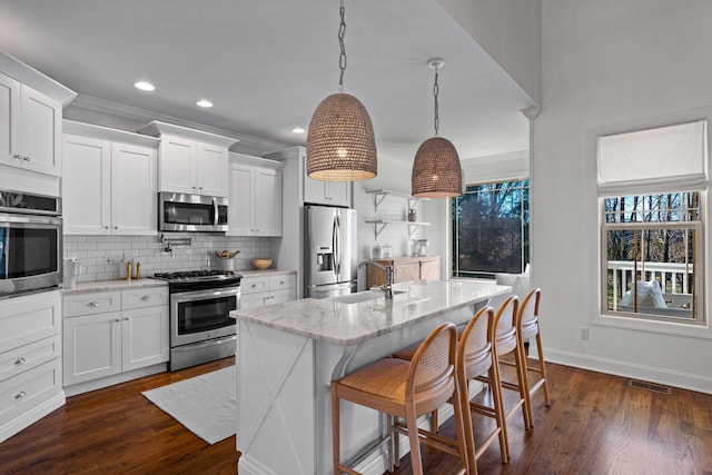 kitchen featuring white cabinetry, appliances with stainless steel finishes, a center island with sink, and hanging light fixtures